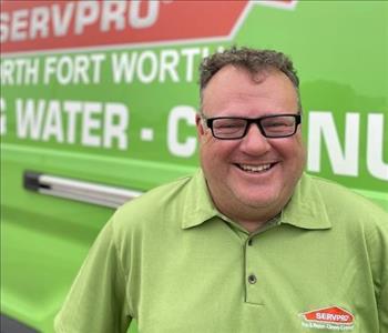 image of person wearing glasses standing in front of green van with Servpro logo
