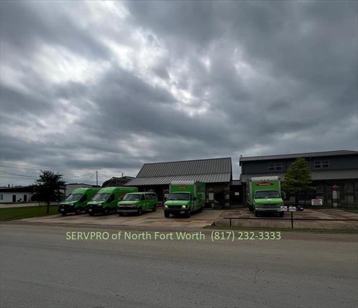 image of five green servpro vehicles and a building with stormy skies overhead