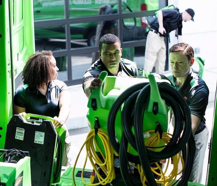 3 SERVPRO employees unloading equipment from their vehicle, with one SERVPRO employee in the background utilizing equipment