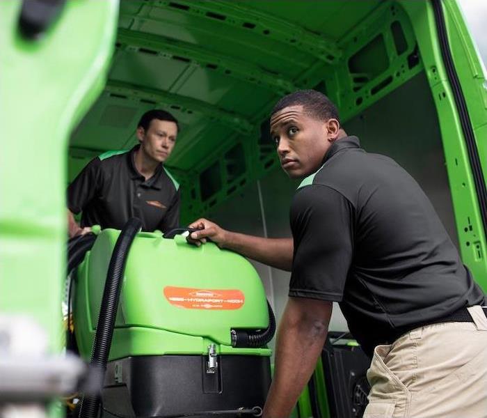 two SERVPRO employees unloading cleaning equipment out of a green van